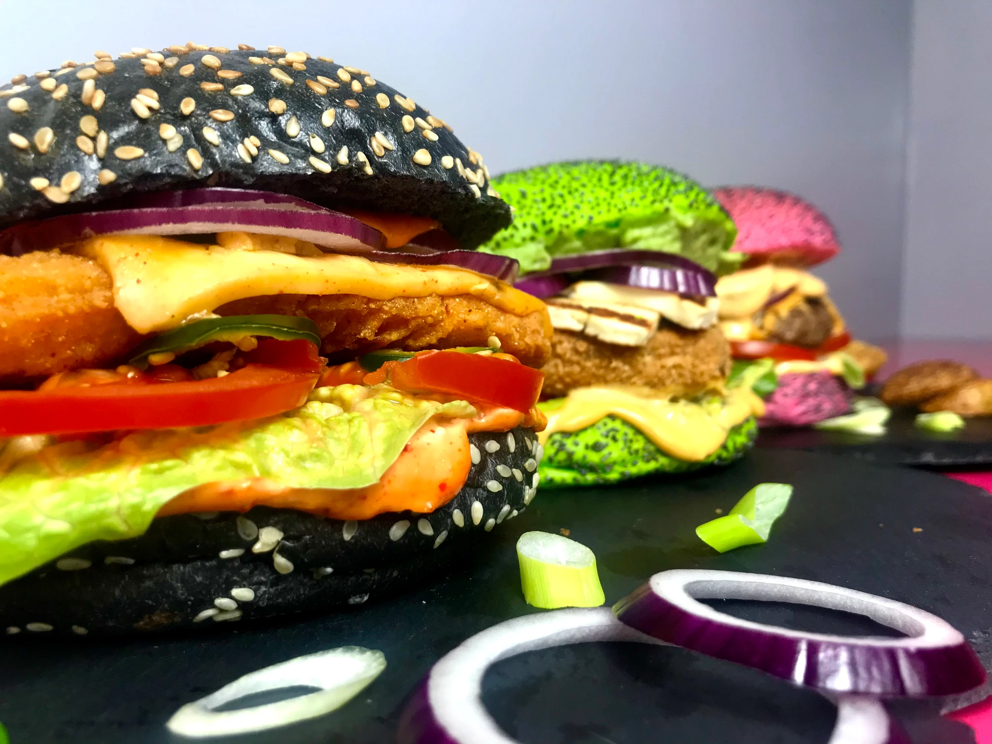 Close-up of burgers with black, green and pink buns